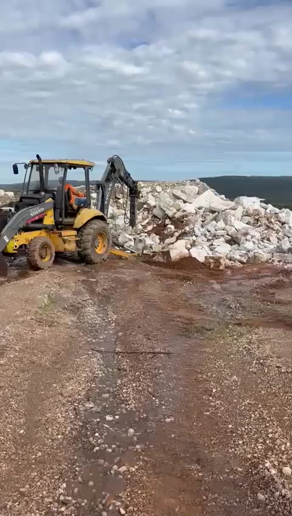 Máquina trabalhando entre blocos claros na frente de lavra em Itacambira