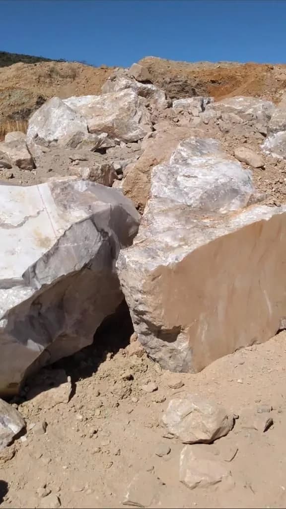 Dois grandes blocos de quartzo recém-extraídos na bancada, com a parede de lavra ao fundo